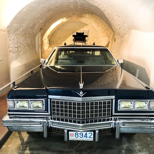 A classic black car with Monaco license plate parked in an arched stone garage.