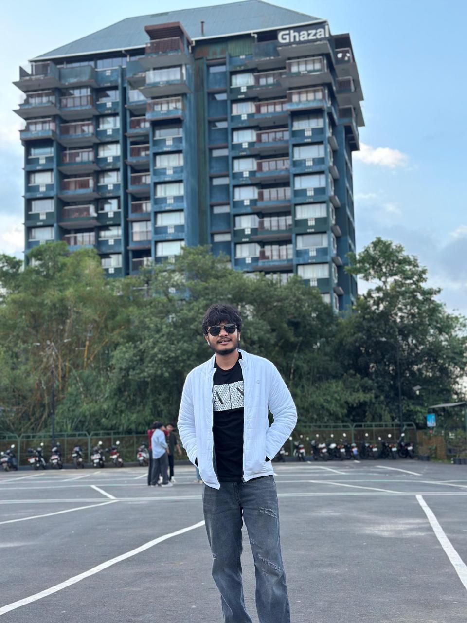 Smiling young man with short hair poses against a dark background, wearing a green button-up shirt.