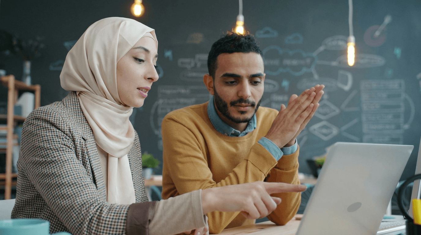 Two Muslim SEO experts and marketing strategists at our halal marketing agency collaborating and reviewing client growth data on a laptop.