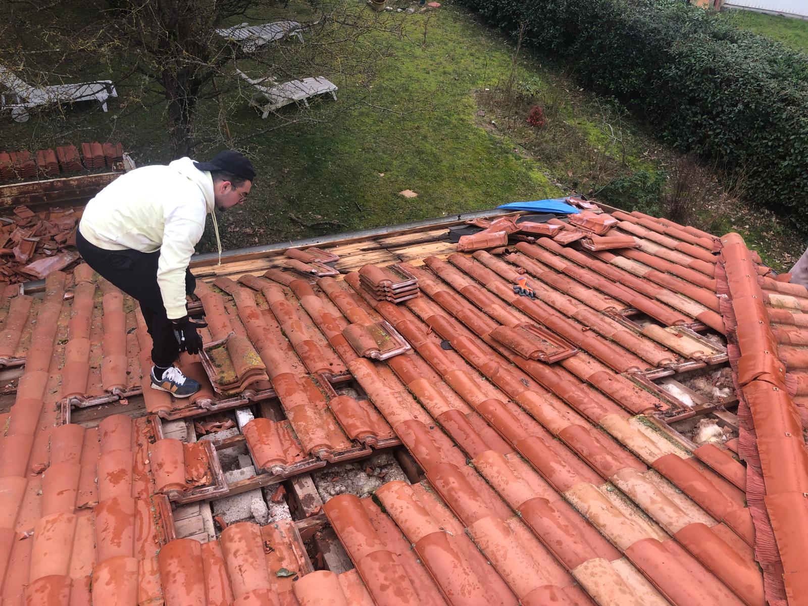 Artisan couvreur professionnel en pleine rénovation d'une toiture en tuiles romanes.