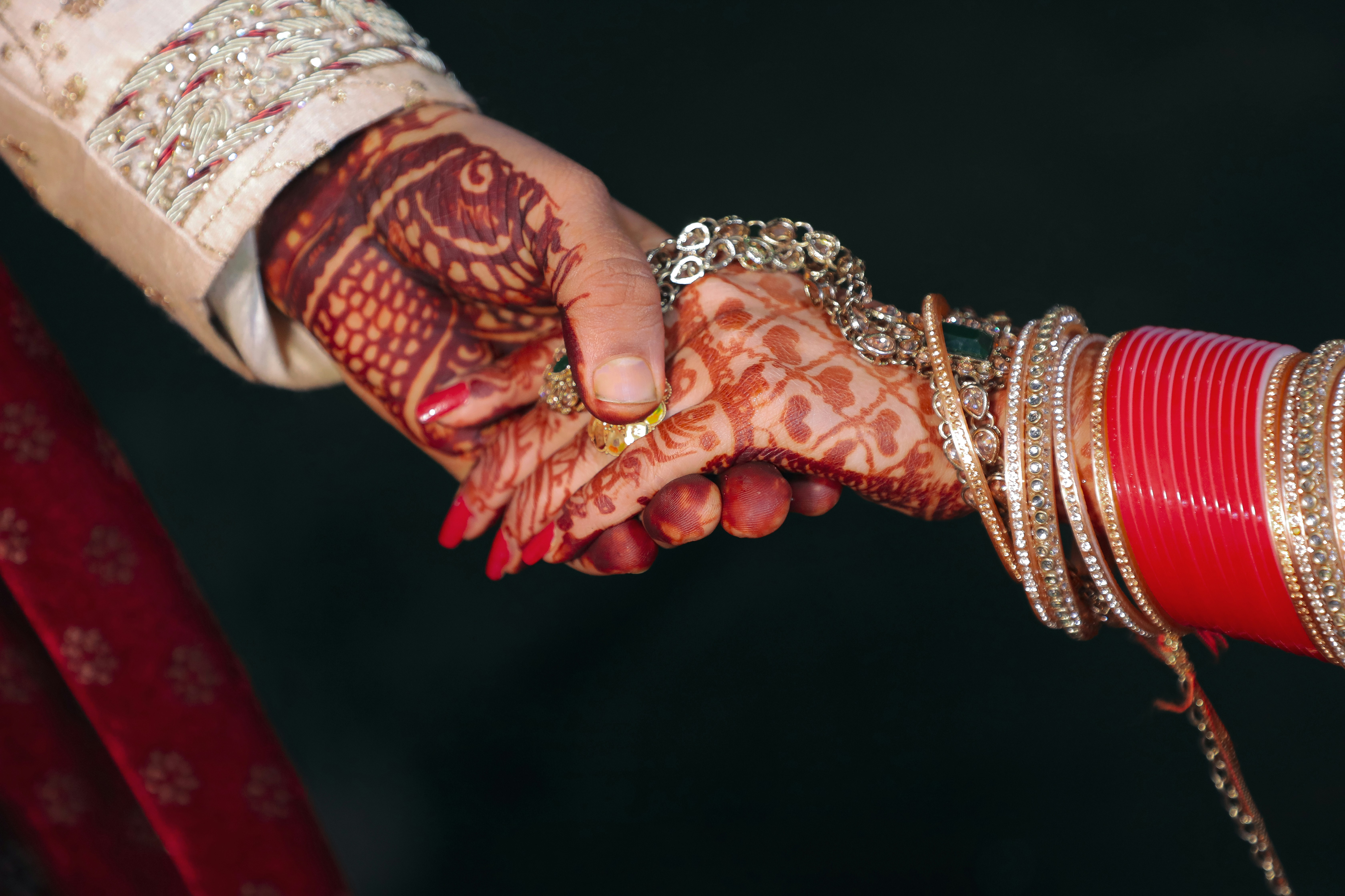 An Indian couple's hennaed hands and bridal bangles clasped together at their wedding