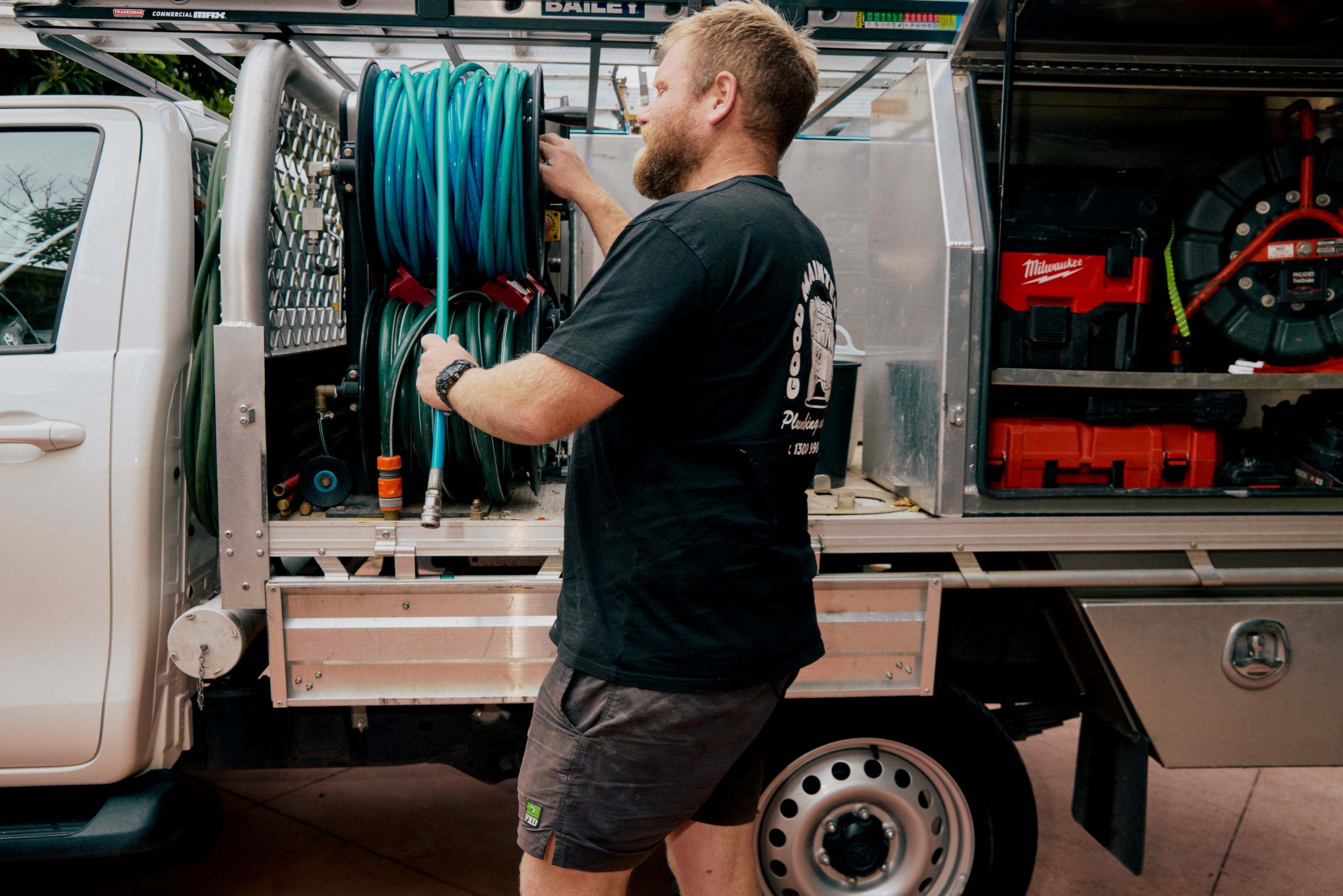 Good Maintenance Tewchnician in company shirt pulling out a hose from the back of a company ute.