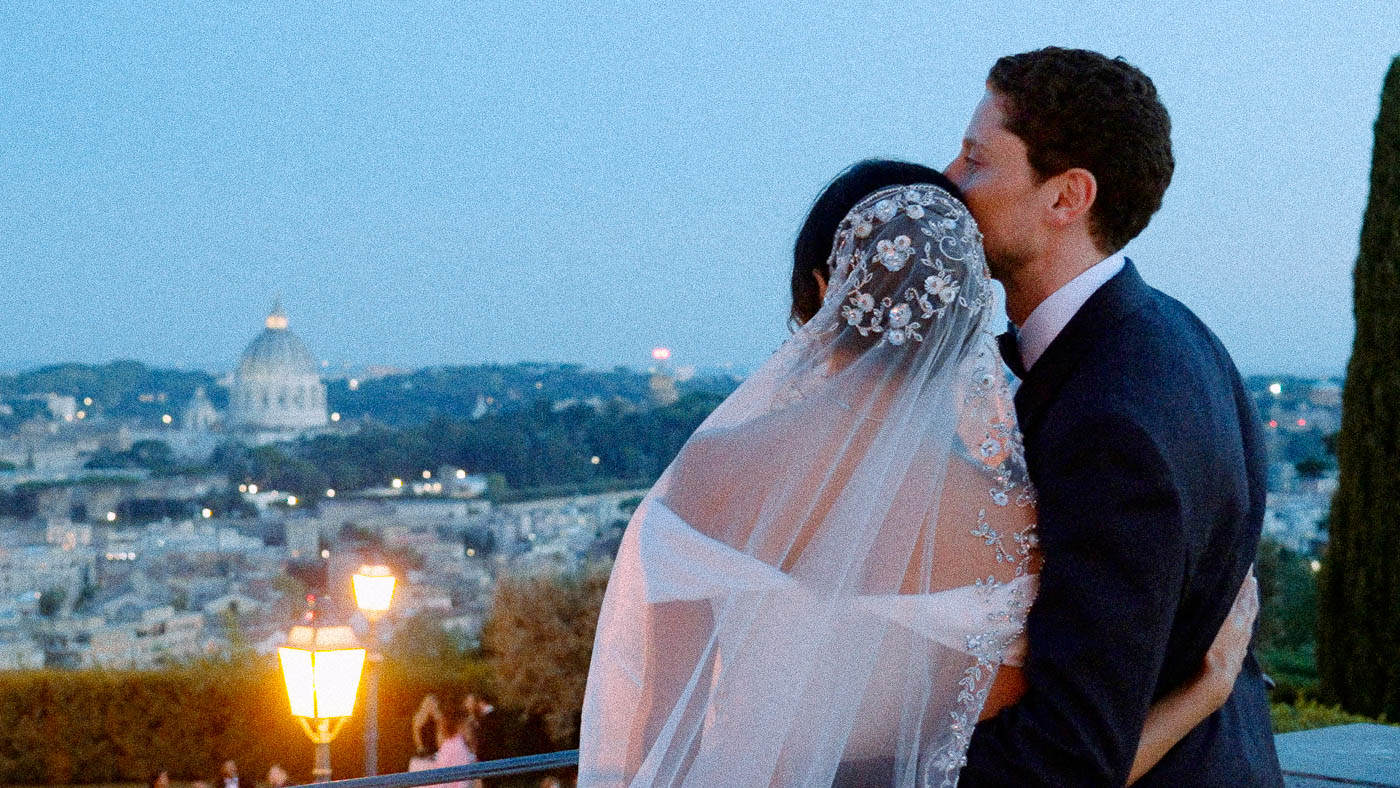 Couple embracing at wedding reception at Villa Miani with panoramic sunset view of Saint Peter's Basilica in Rome.