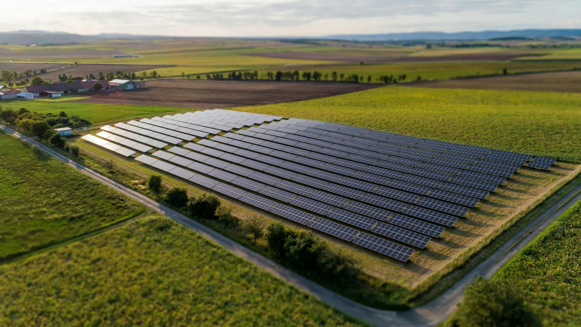 Aerial view of a utility-scale solar farm surrounded by green farmland and a winding road