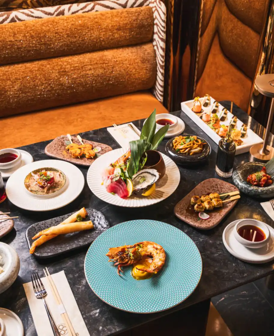 Sushi Club Porte Maillot 的餐桌:刺身、生蚝、炙烤甲壳海鲜与烤串,背后是琥珀丝绒长椅