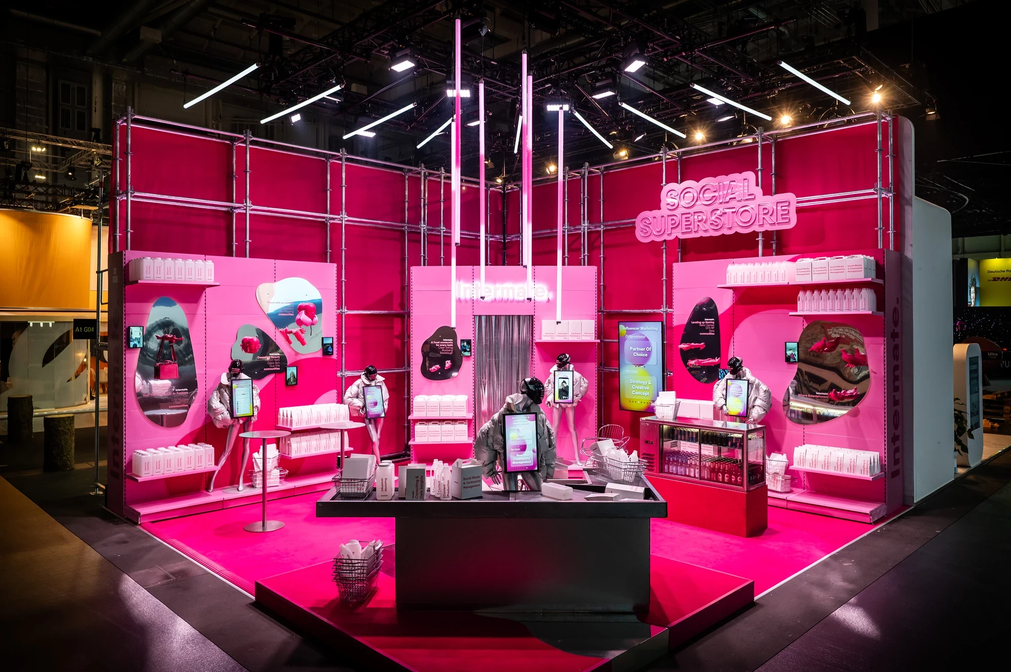 Intermate „Social Superstore" booth in bright pink with neon signage, scaffolding-style shelves, screens and product displays.