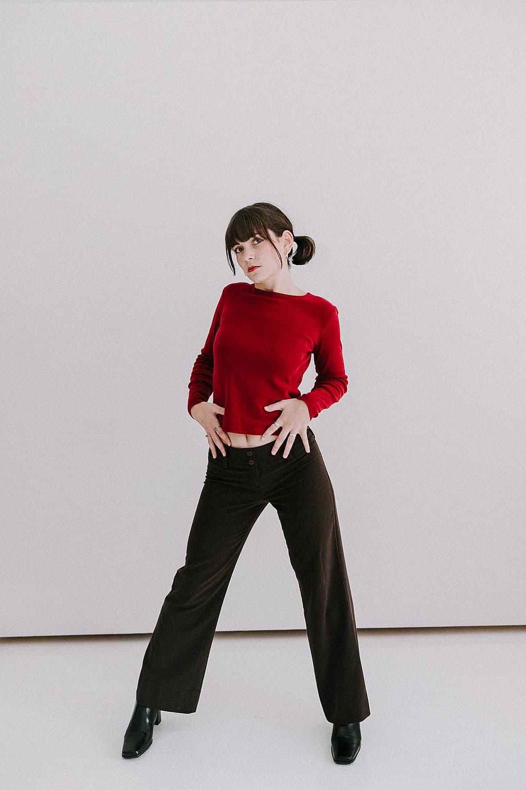 A model standing in a power pose wearing a red sweater and brown pants, embodying 90s vintage fashion at Revelator Studio, a natural light studio in Shreveport.