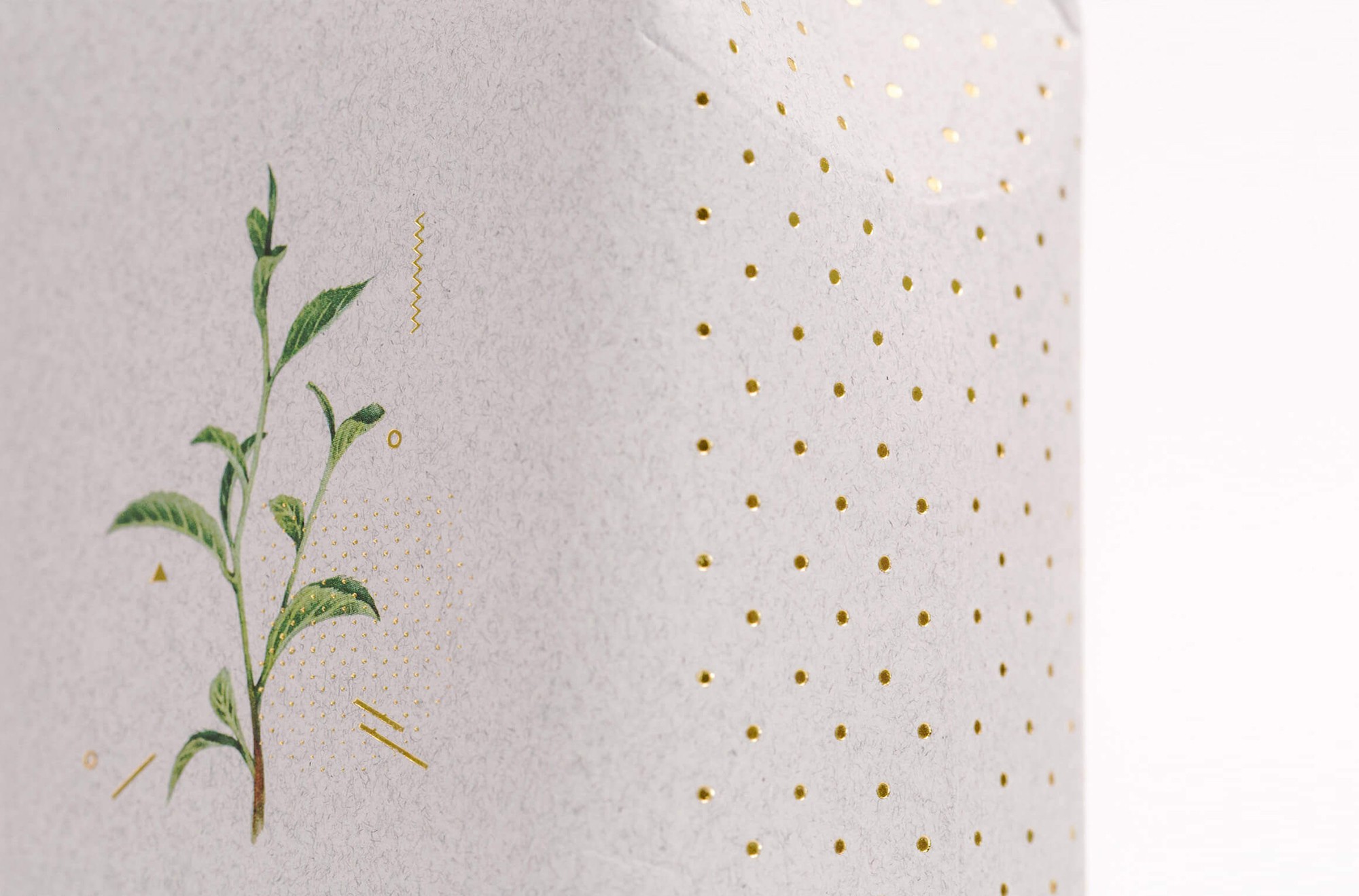 這張圖展示了清山寶珠的包裝細節。包裝紙材質上印有一株茶葉的手繪水彩插圖，背景上點綴著金色的小點和幾何圖形。