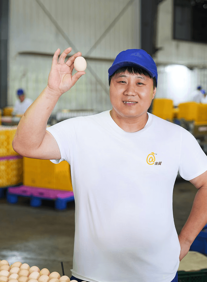 一位戴着蓝色帽子的金翼食品员工面带微笑,自豪地展示着一枚新鲜鸡蛋,象征着优质蛋品。