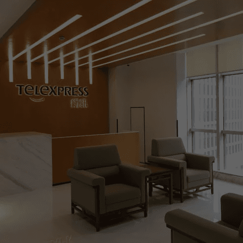 A modern hallway features vibrant teal and orange geometric and leaf patterns, with glossy tiled floors, a large rectangular light fixture, and a small shelf holding a potted plant, all leading to a large, frosted window at the end.