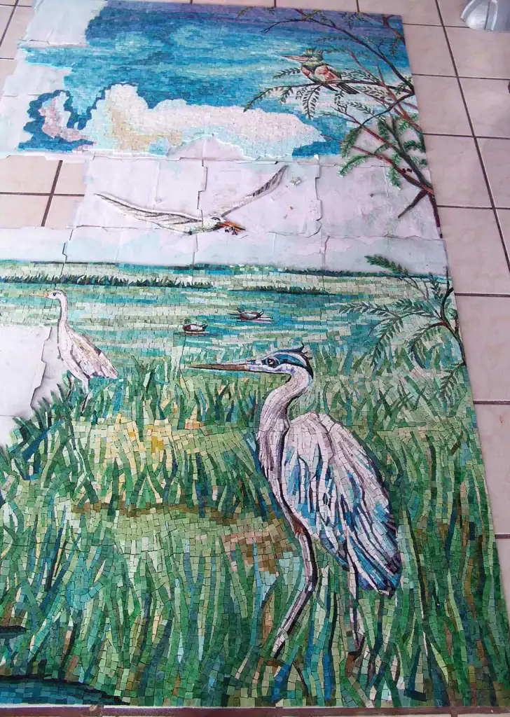 Detailed mosaic artwork of herons in a marshland setting with sky and clouds.