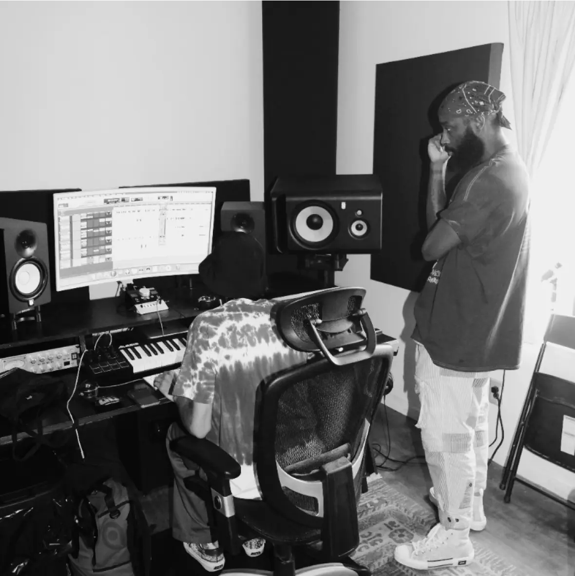 A soundtrack producer collaborates with an artist in a music studio, using audio software to work on a project.