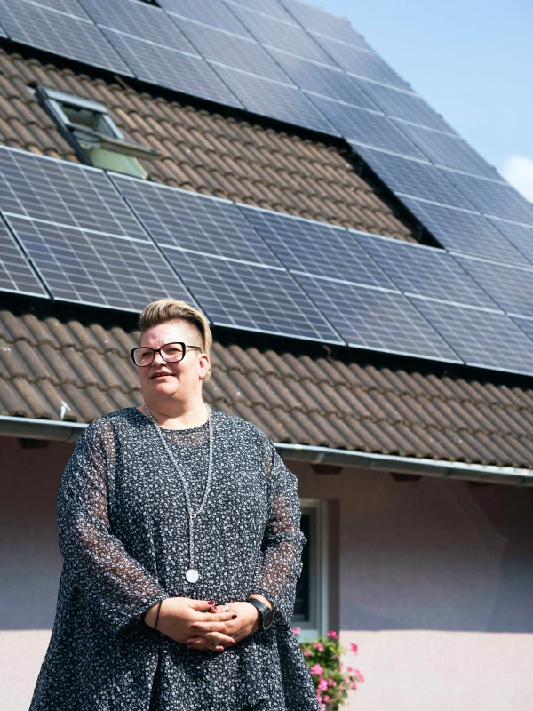 Eigentümerin vor ihrem Haus mit fertig installierter PV-Anlage auf ihrem Dach
