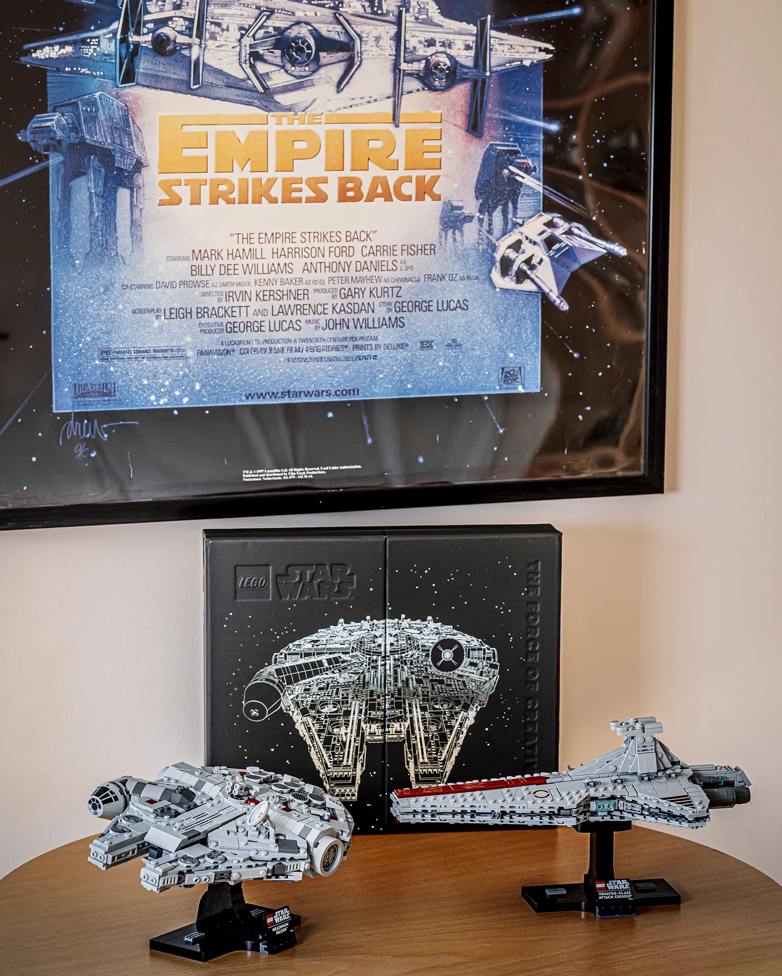 LEGO® Star Wars modeller av "Millenium Falcon" & "Venator-class attack cruiser" utstilt på bord med LEGO Star Wars bok og en film plakat i bakgrunn