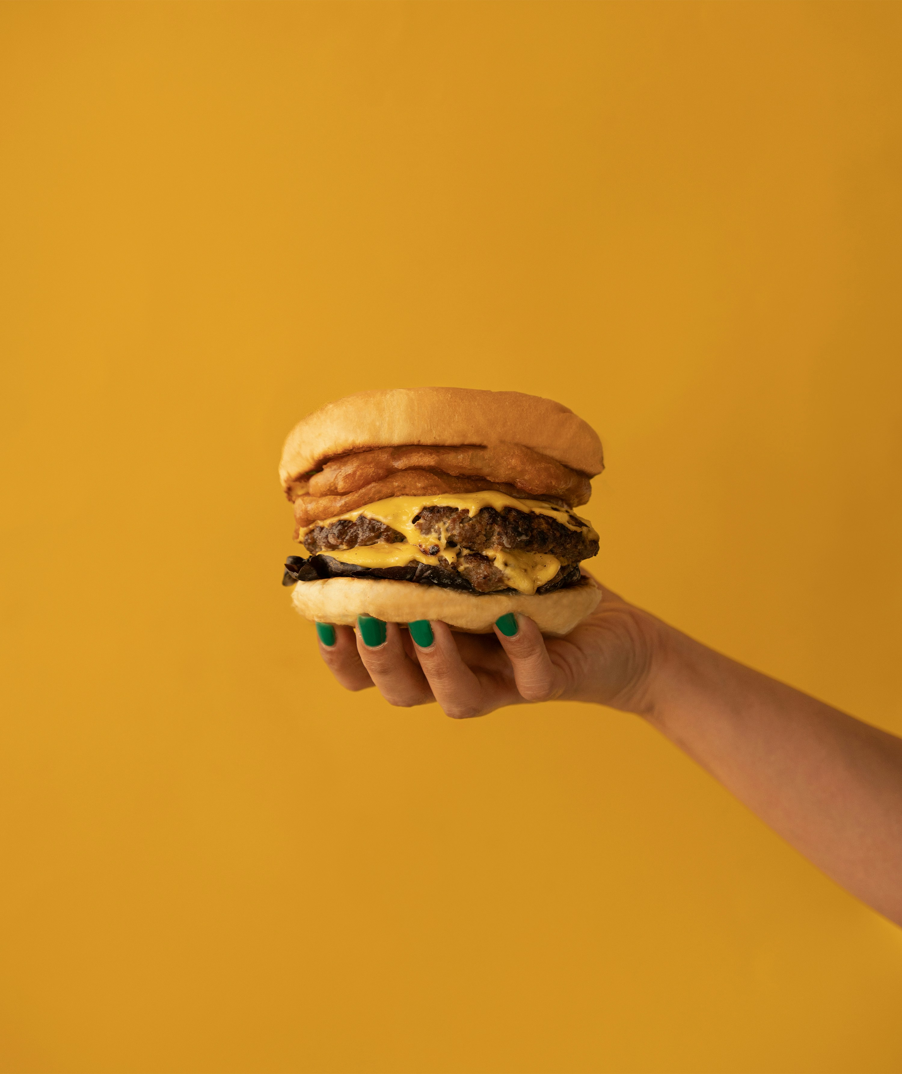 a hand holding a cheeseburger on a yellow background