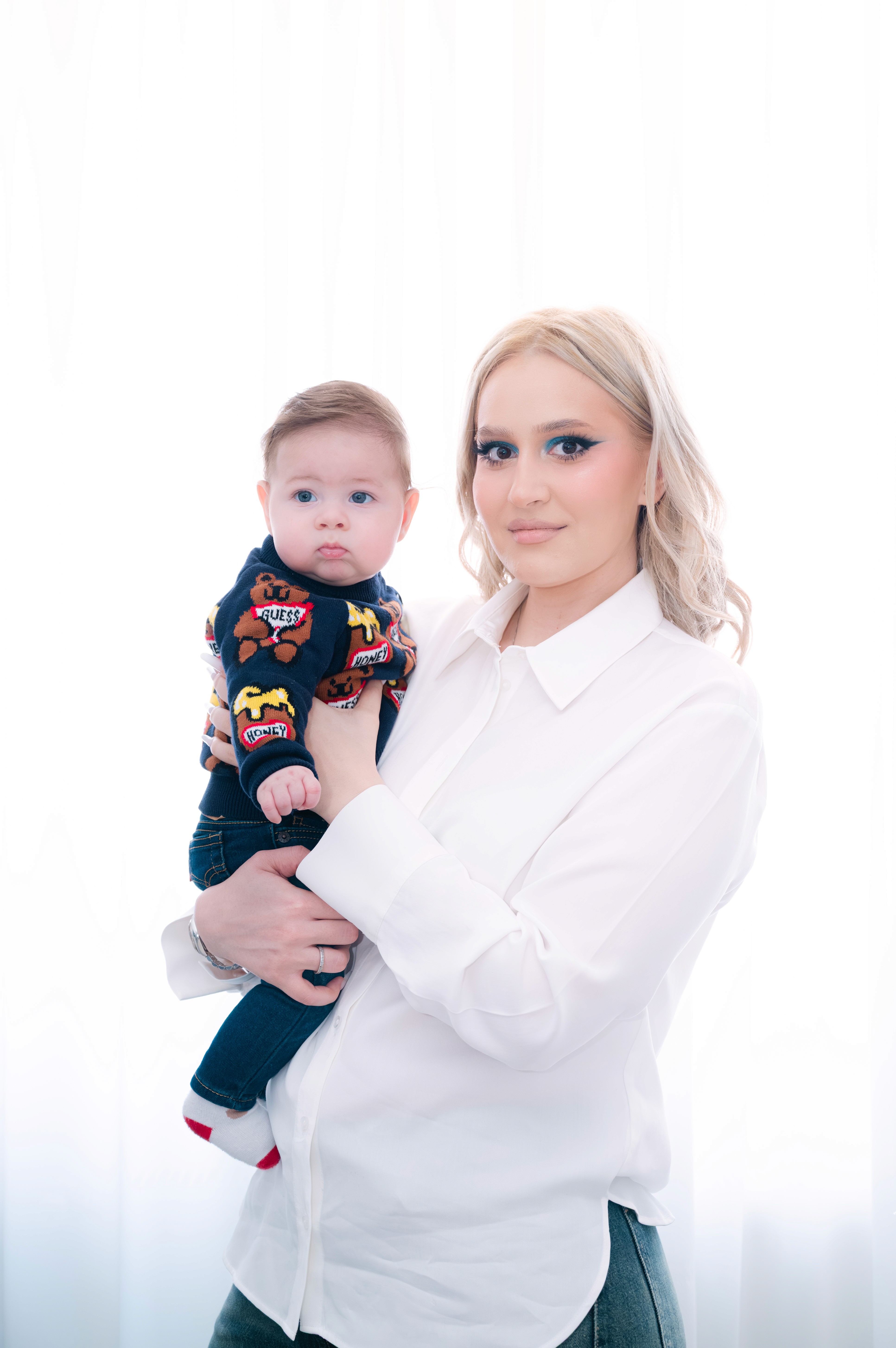 Mamă ținând în brațe bebelușul îmbrăcat pentru botez, portret luminos de familie.