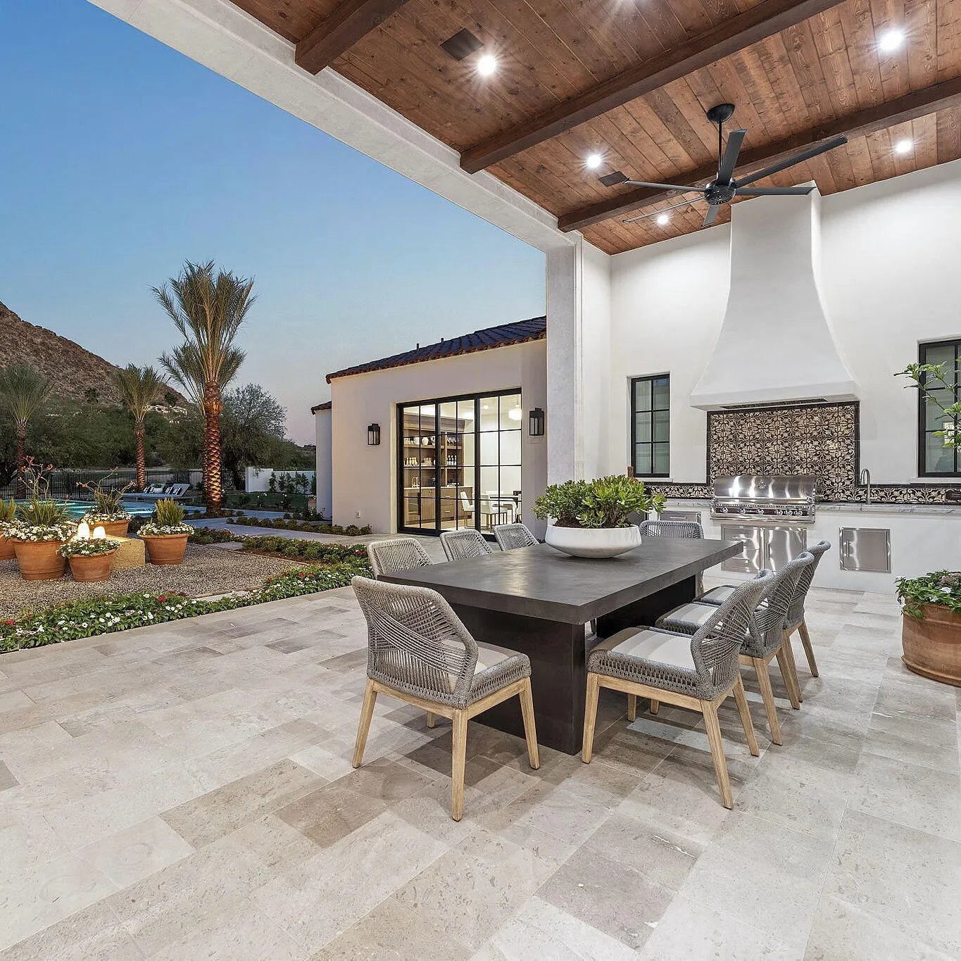 Outdoor patio with a wooden dining table and chairs, surrounded by desert landscaping and a modern house facade.