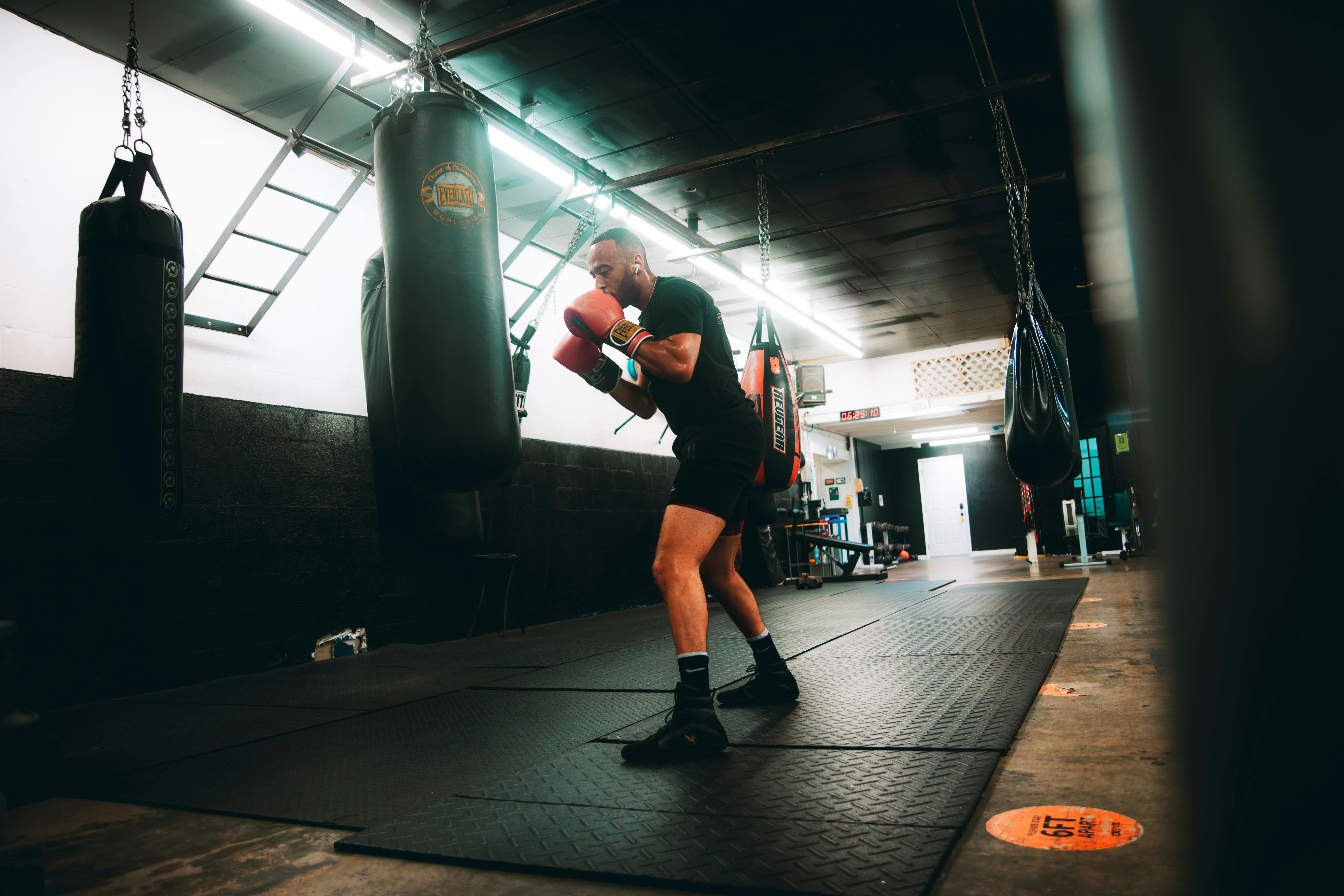 Male boxer with red gloves training with a punching bag in a gym.