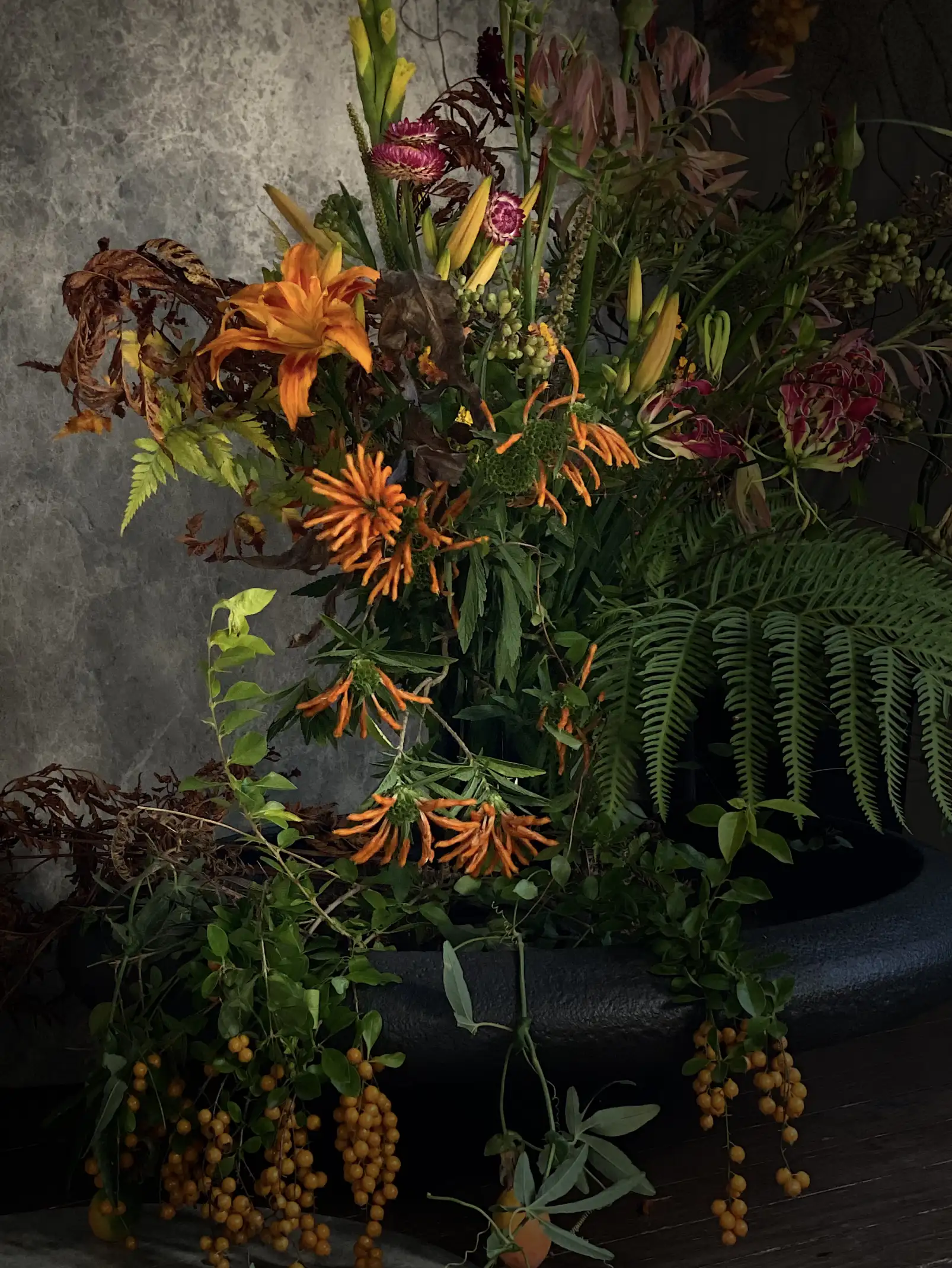 Arreglo floral con lirios y follaje verde en maceta negra para instalación decorativa con inspiración silvestre.