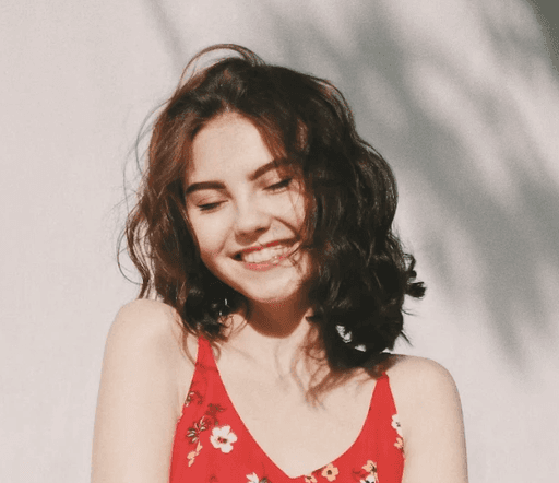 Jeune femme brune dehors devant un mur blanc