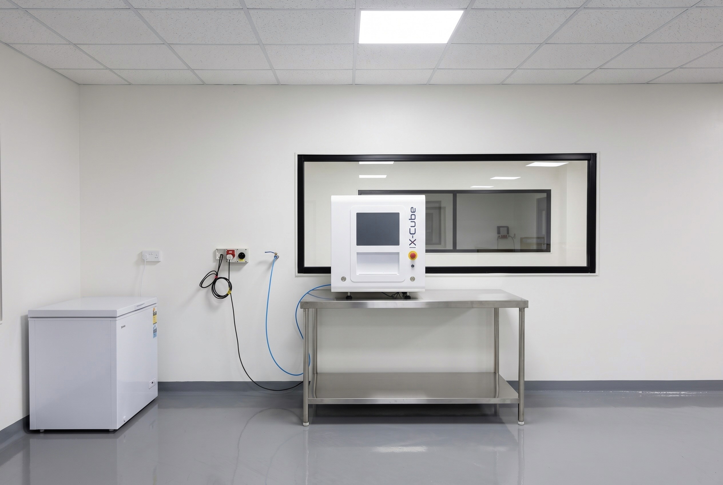 A Schneider X-Cube laser engraving machine on a workbench in the Afrilens plant, with the stock room visible through an interior window.