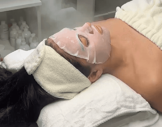 A woman relaxing in soft sunlight, surrounded by plants and warm decor, emphasizing the peaceful and rejuvenating experience of the spa.