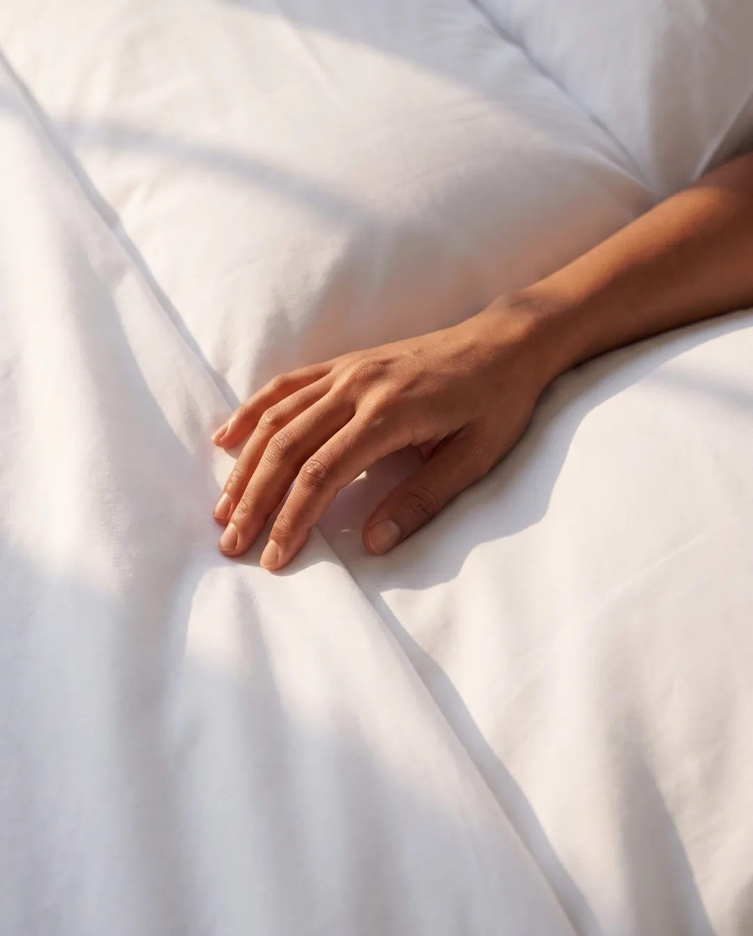 Hand resting on white hotel bedding