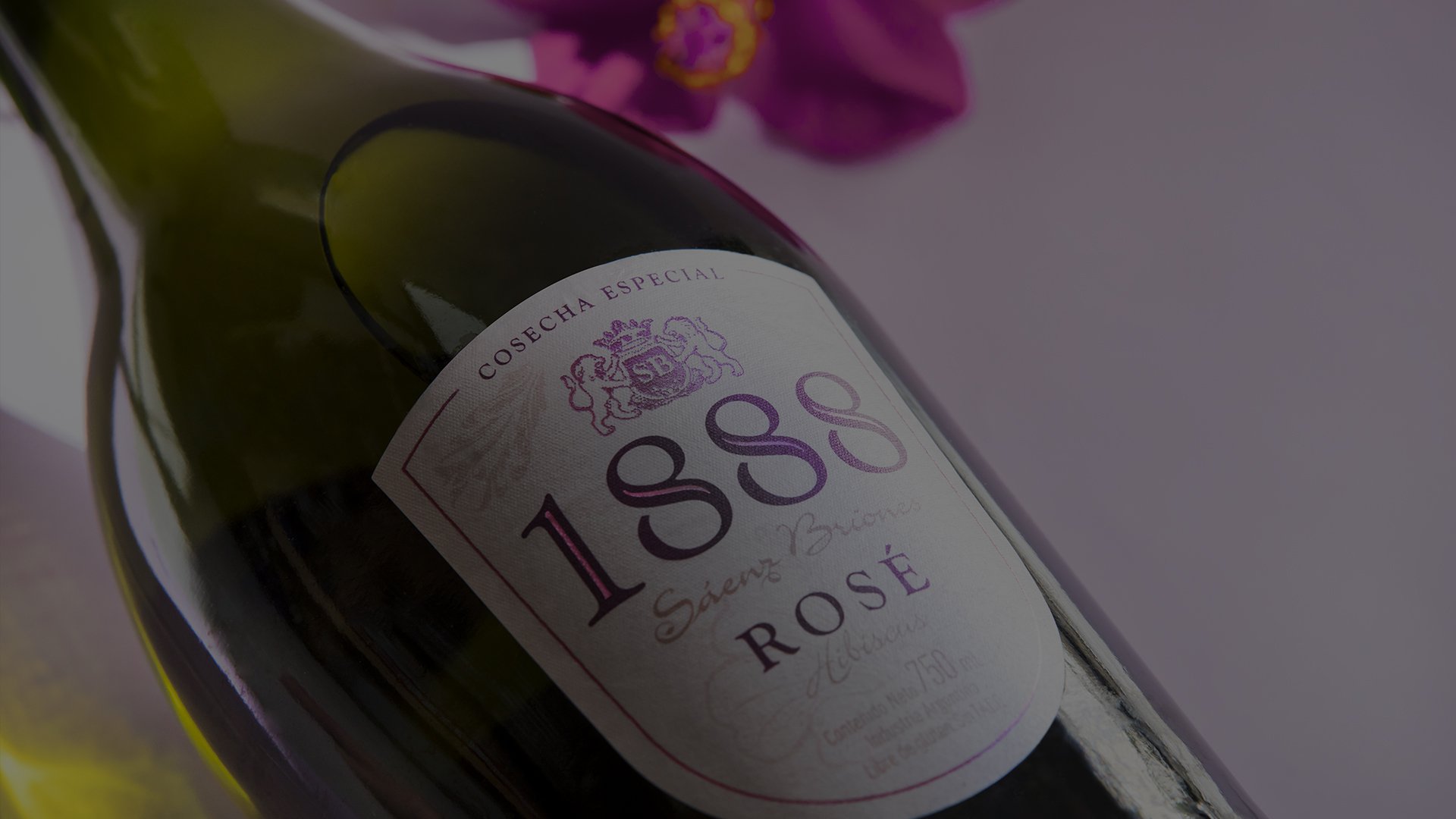 A bottle of 1888 rosé wine lies on its side, featuring a classic label with elegant typography. A vivid pink flower is blurred in the background.