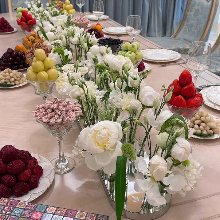 Formal dining table with white floral centerpieces, assorted fruits, and elegant gold-trimmed plates