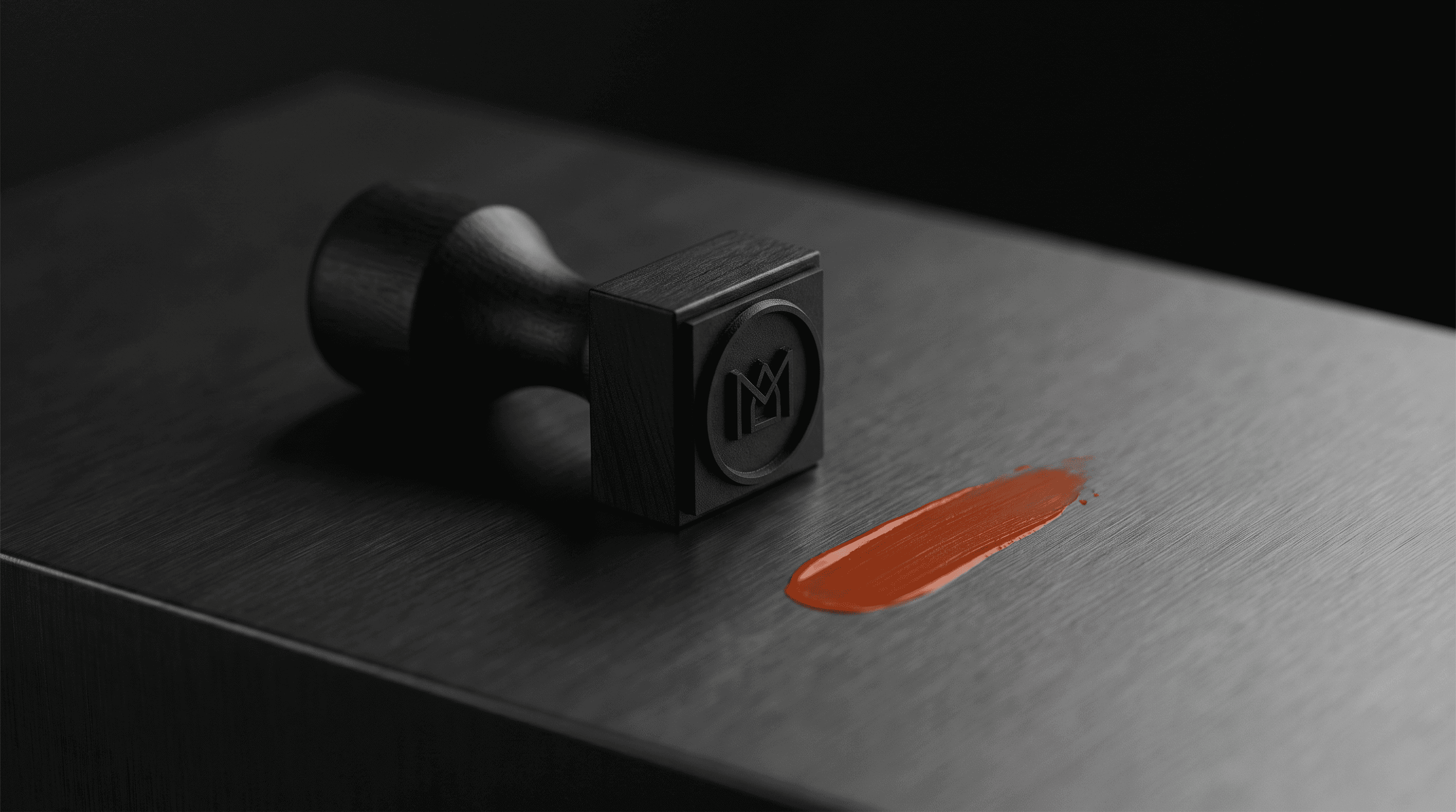 A black rubber stamp with a monogram lying beside a smear of orange ink
