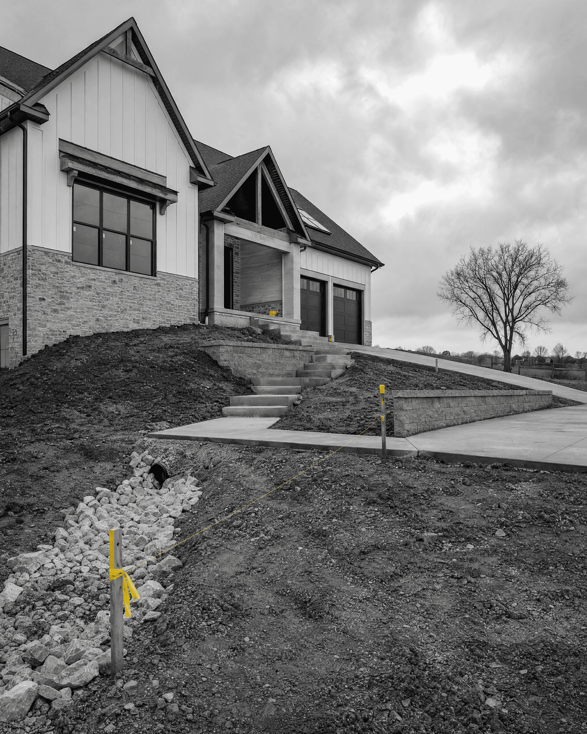 Residential property on a sloped site with exterior steps, retaining wall, driveway, and a rock-lined drainage channel.