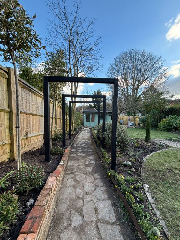 "Natural stone pathway lined with multiple decorative black metal garden arches in Marlow