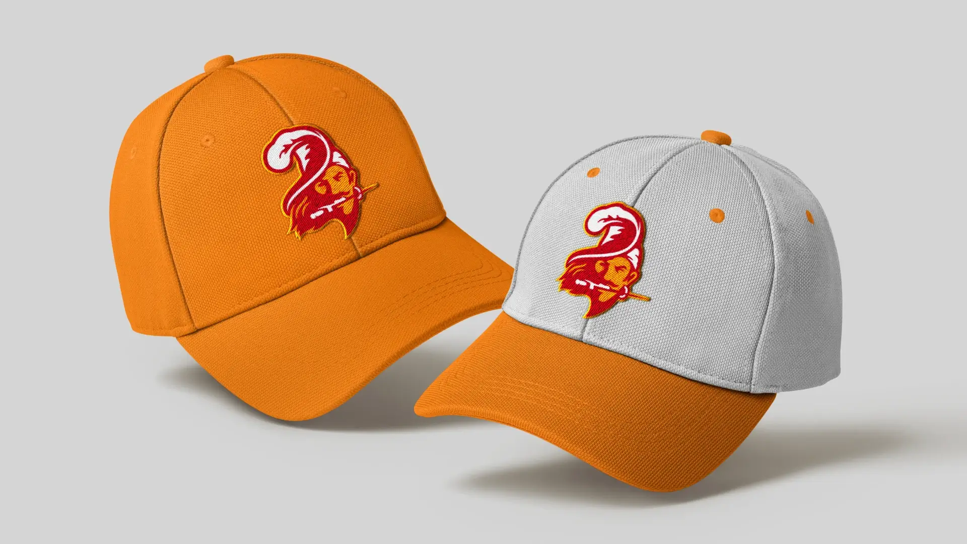Two hats floating on a gray background with the new buccaneers logo embroidered. One is light orange and the other is white with an orange brim.