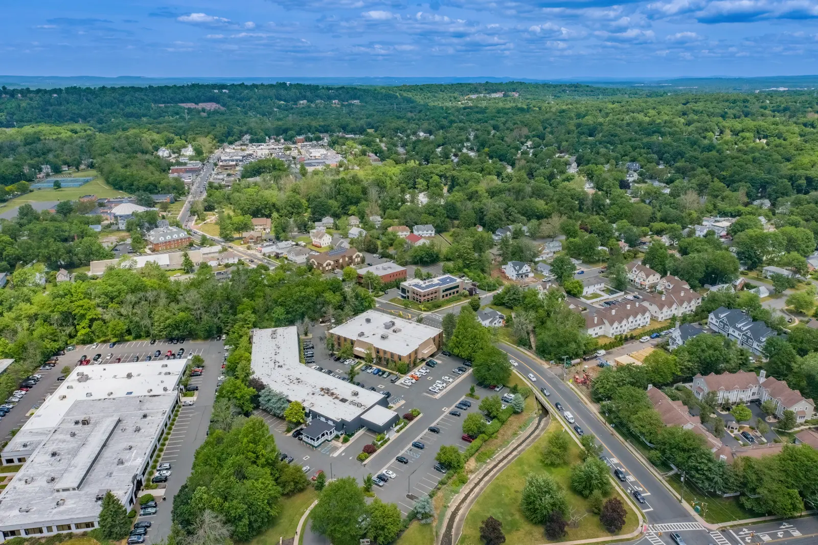 Aerial view of a green suburban town with buildings, roads, and homes.