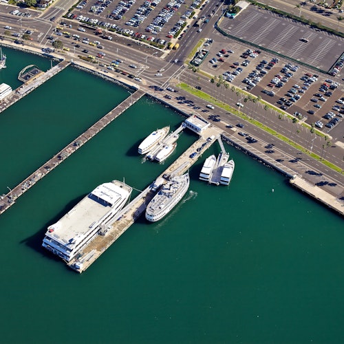 Vista aérea de una marina con muelles, varios barcos atracados y estacionamientos adyacentes llenos de coches.
