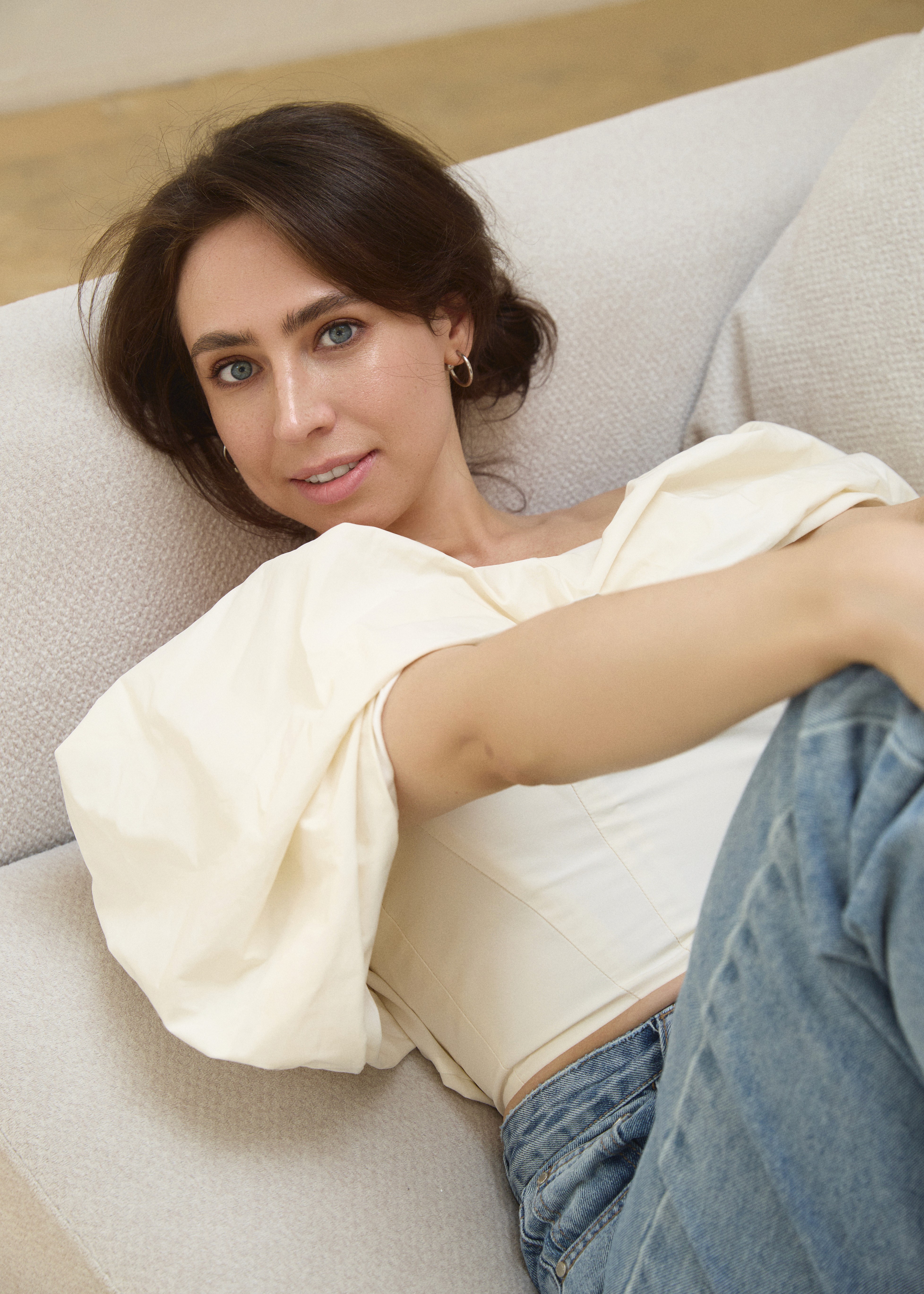 Woman relaxing on a light sofa, wearing a white top and jeans
