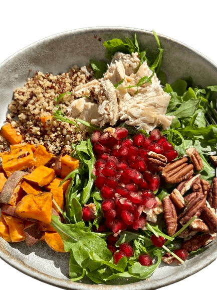 nourishing salad with roasted sweet potato, quinoa, rotisserie chicken, pecans, arugula, and pomegranate arils in a light tan bowl plate