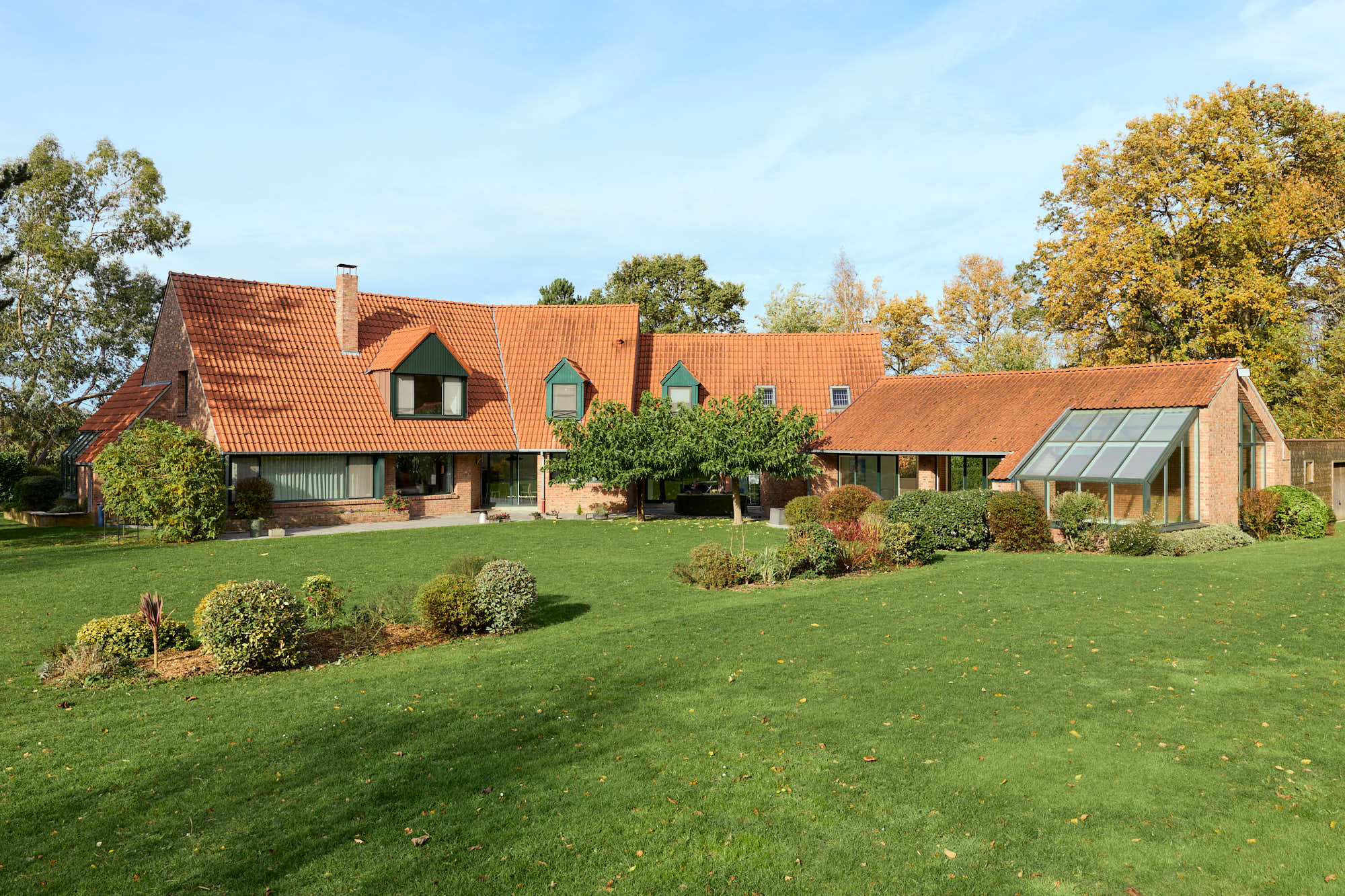 Grande maison avec un grand jardin bien entretenu et deux îlots floraux par temps ensoleillé.