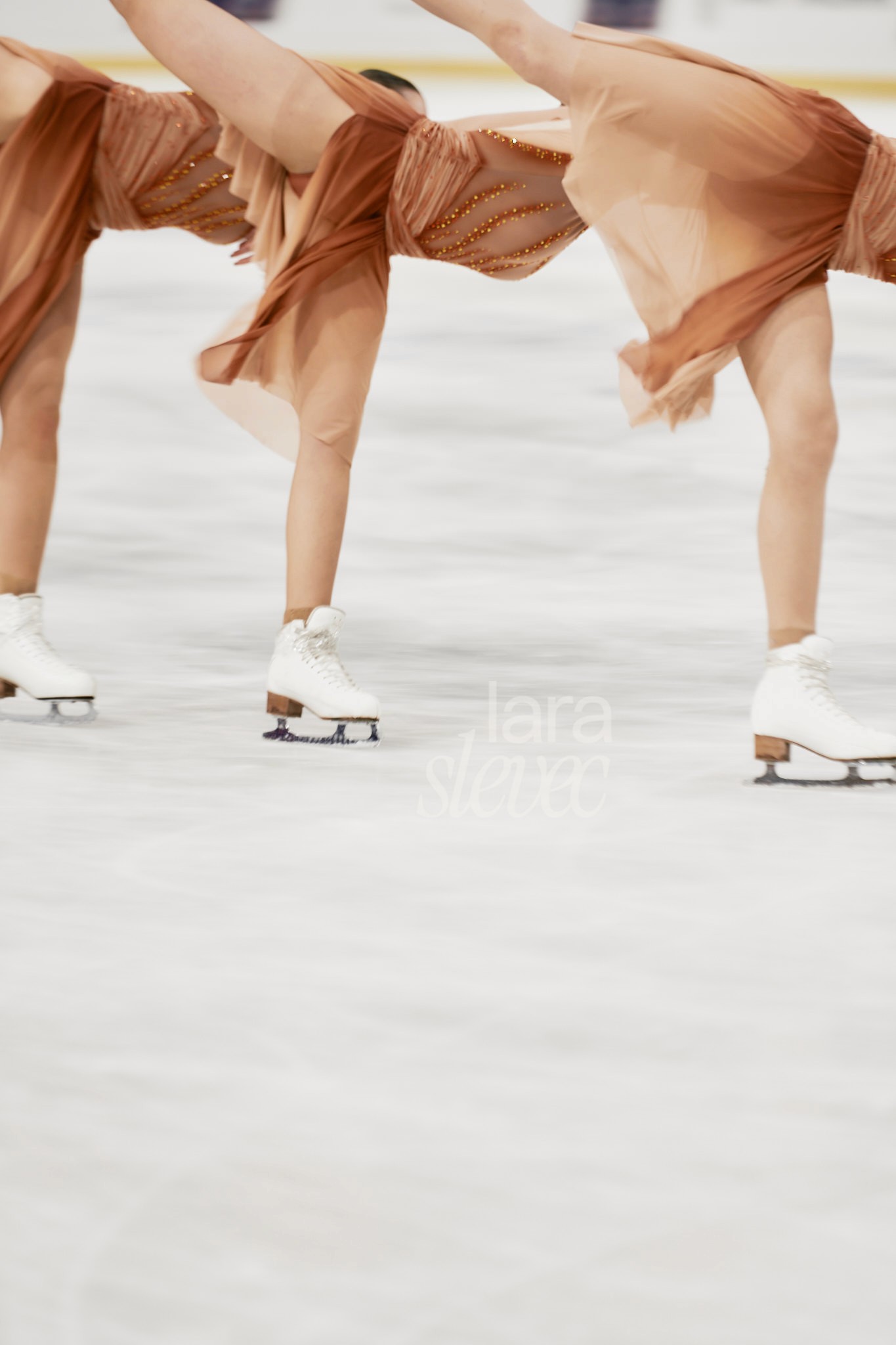Im oberen Bilddrittel sieht man drei Synchroneiskunstläuferinnen, die gerade einen Flieger zeigen. Sie sind leicht in Bewegungsunschärfe. Team Ice on Fire. ISU Synchronized Skating Championships 2026 in Salzburg. Fotografiert von Lara Slevec.