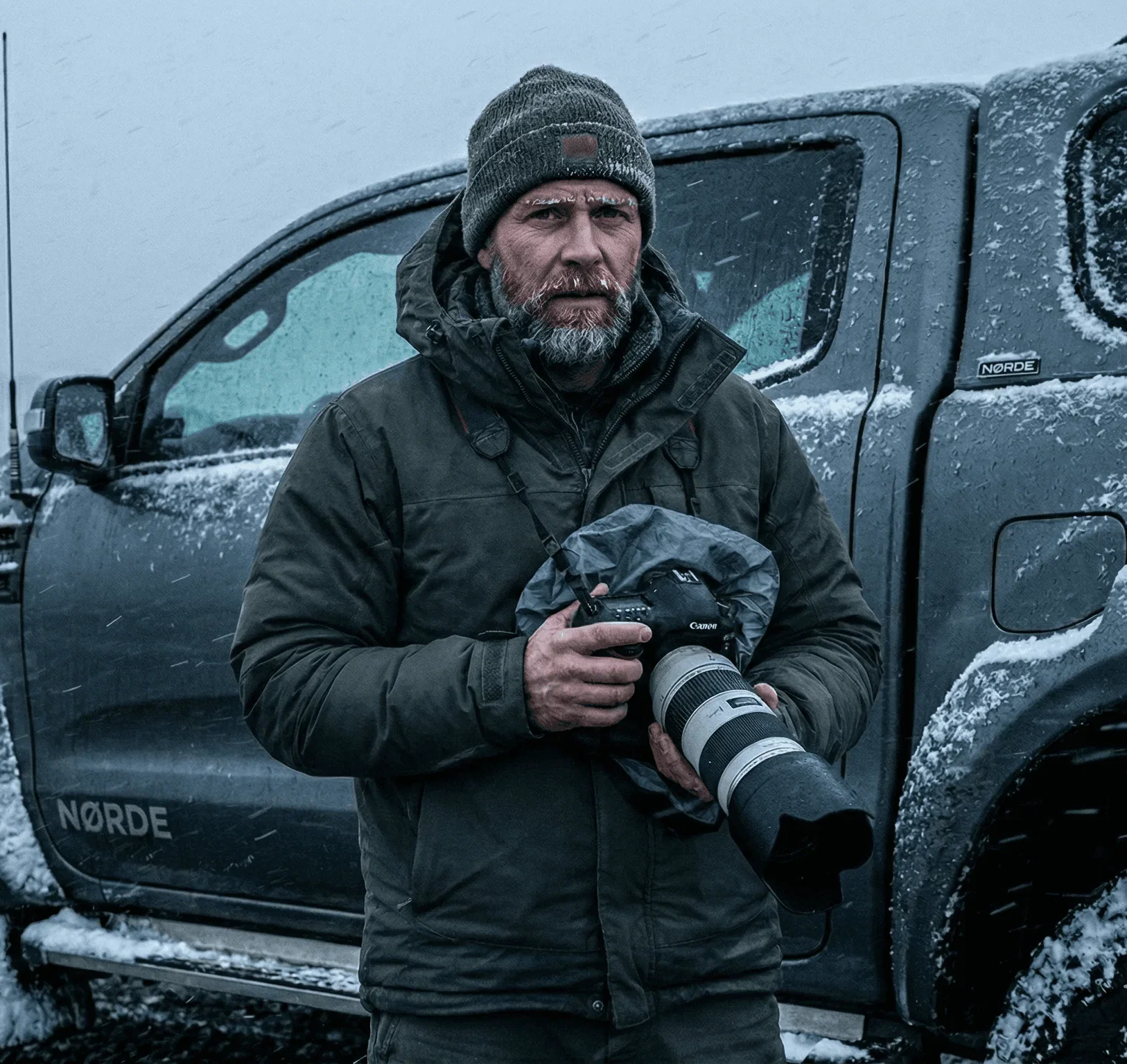 Bearded man holding a camera in a snowstorm.