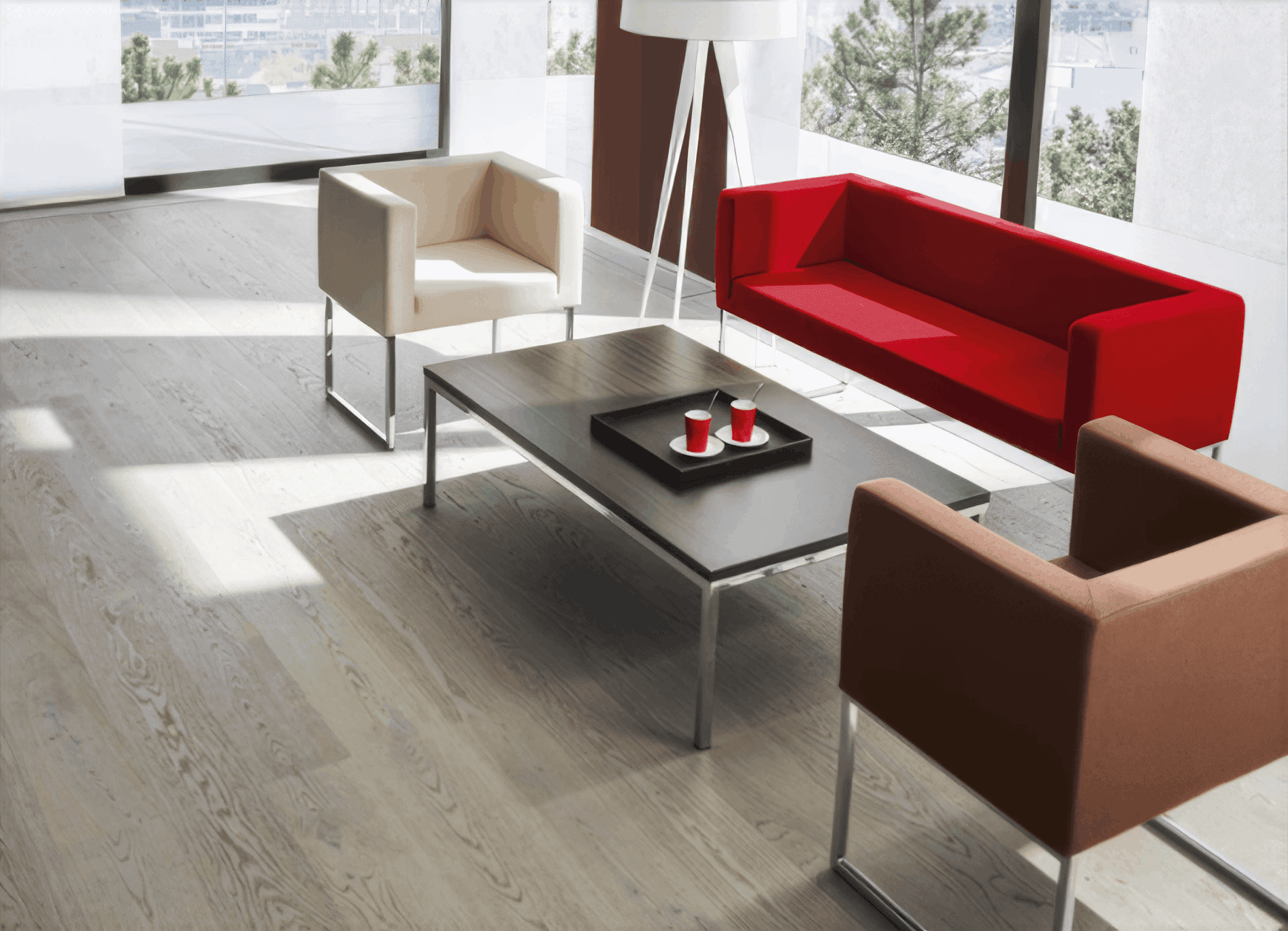MW Interior - Moderne Bürolounge mit rotem Sofa, cremefarbenem und braunem Sessel auf Chromgestell, dunklem Couchtisch und Parkettboden" Beschreibung: Einladende Wartezone mit kubisch geformten Polstermöbeln in Rot, Creme und Braun auf elegantem Echtholzparkett – klare Formen, starke Farbakzente und ein stimmiges Gesamtbild für Empfangs- und Loungeflächen.
