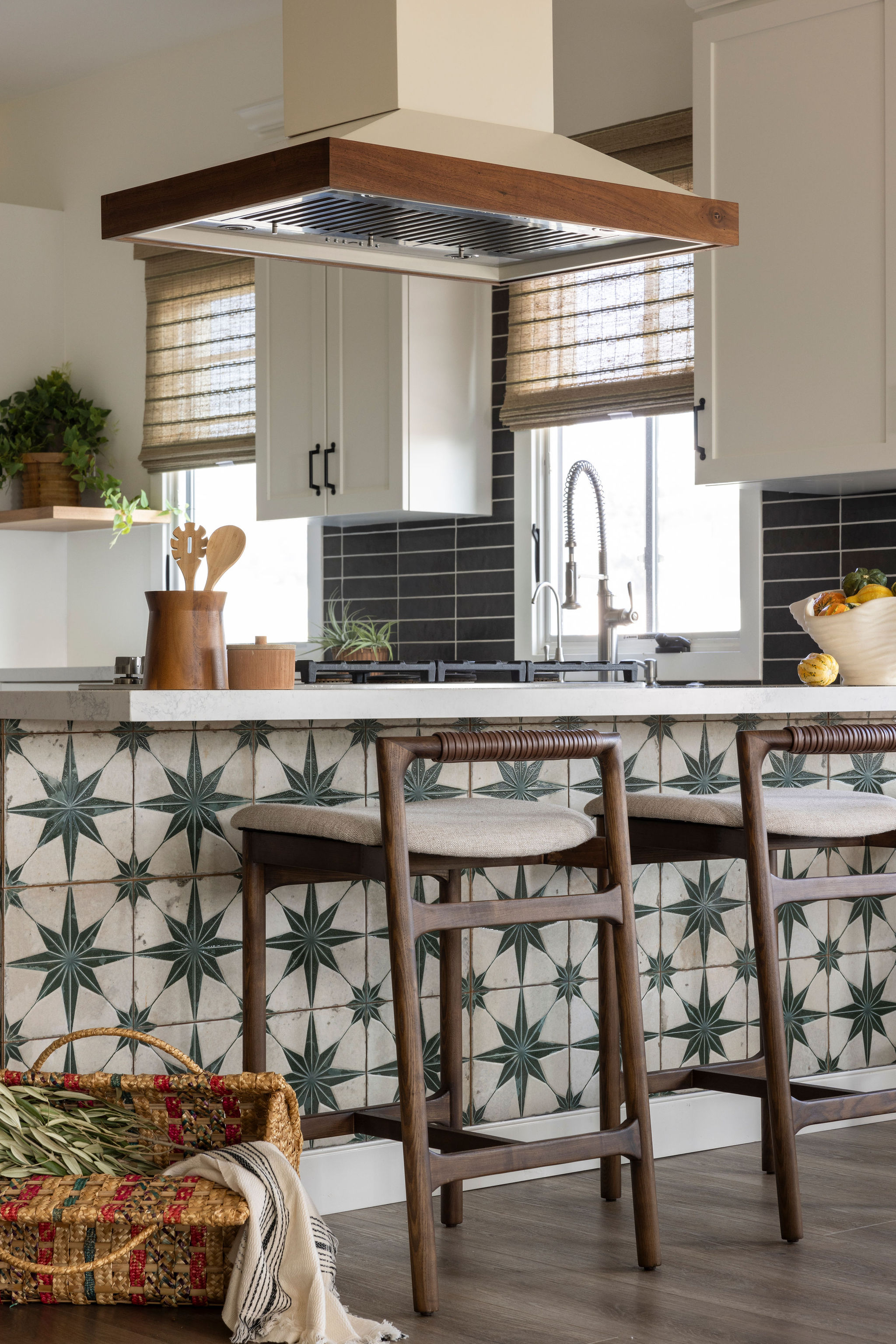A modern kitchen blending coastal charm with unique design elements like a custom hood with warm wood accents, wood and leather bar stools, and a stunning green star tile detail on the island.