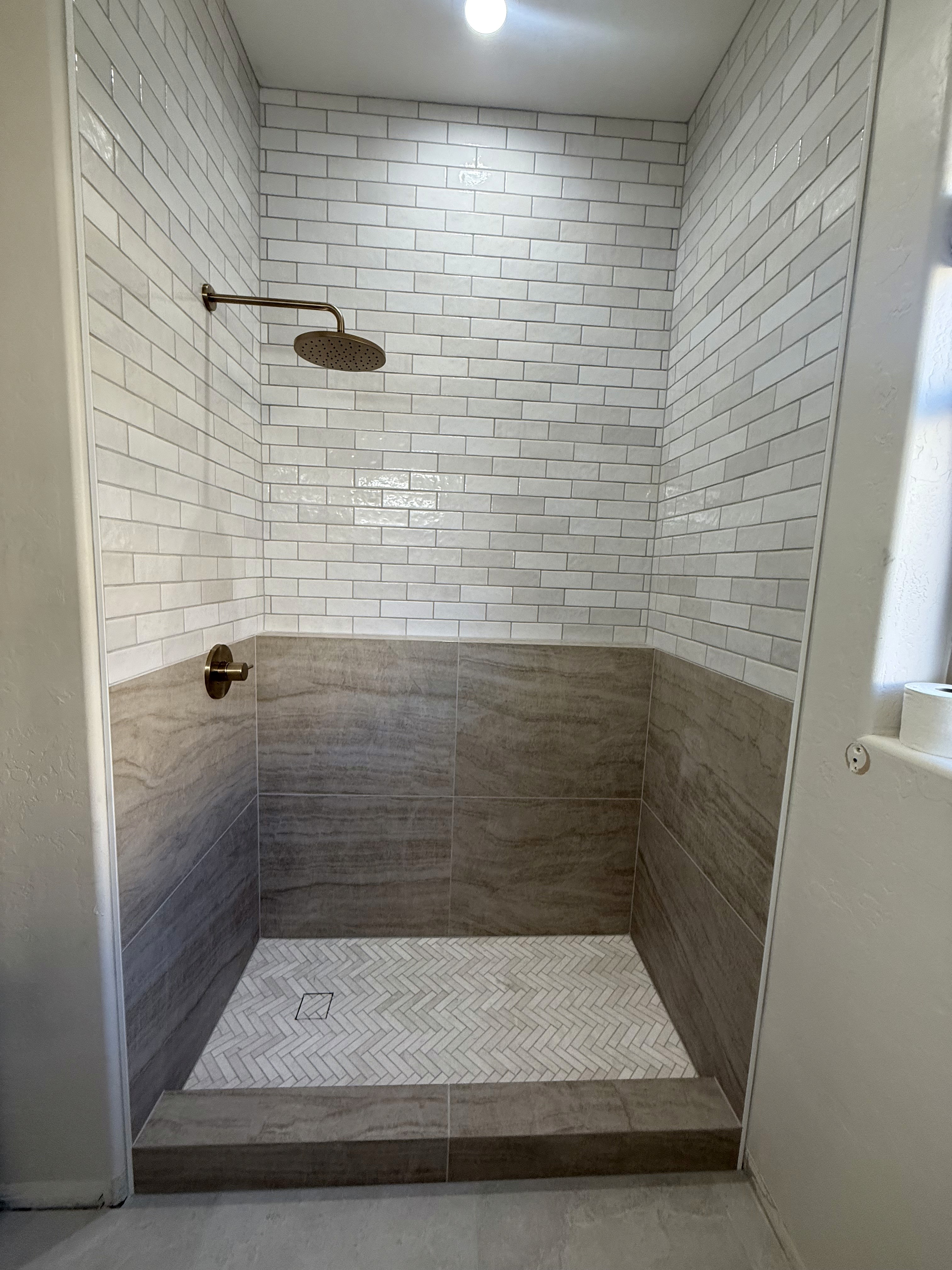 Modern shower featuring textured white wavy wall tiles, two built-in niches with dark grey subway tile inserts, a vertical accent stripe of dark grey subway tiles, and a multi-toned pebble mosaic shower floor.