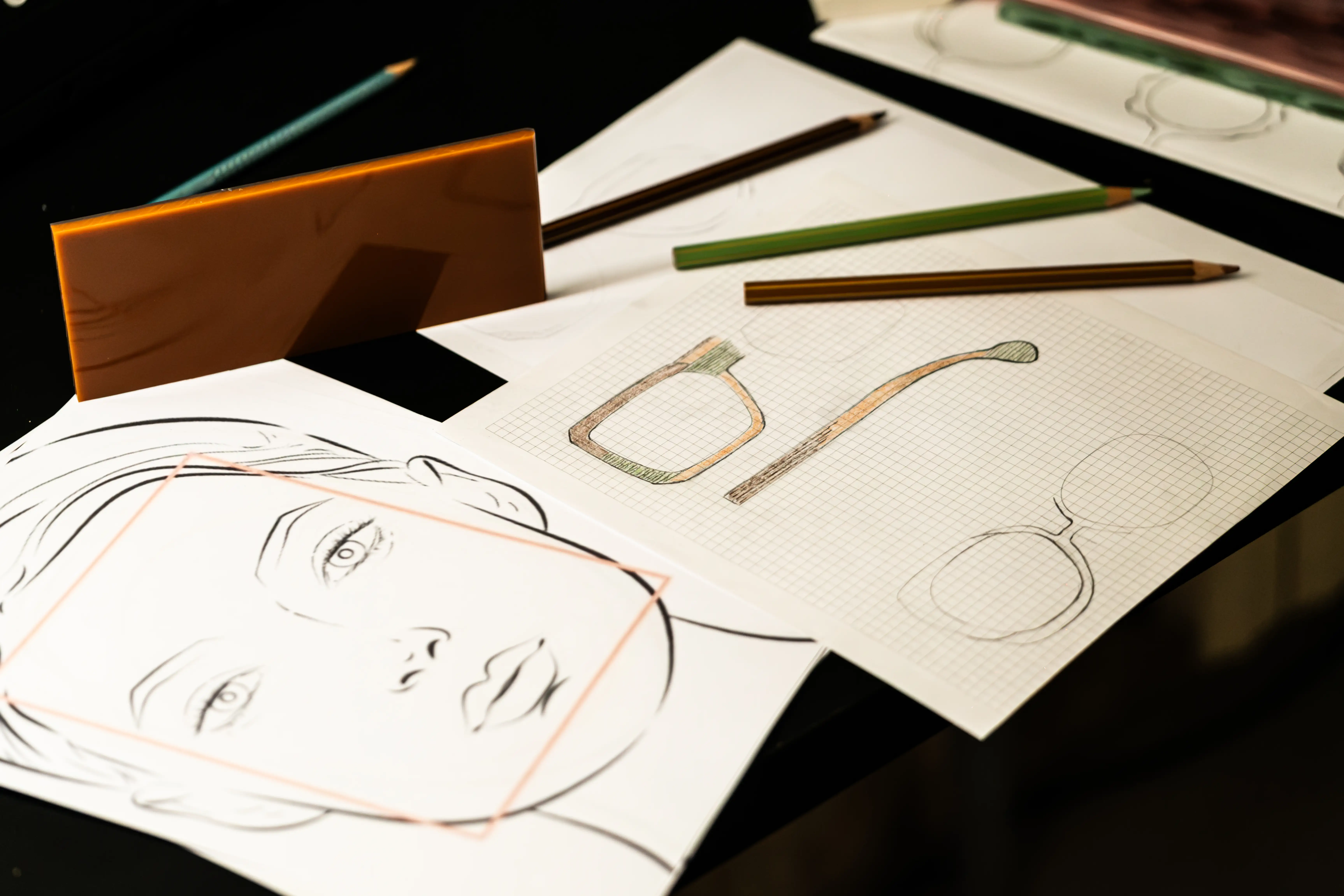 Progettazione di un occhiale IDIA su misura di Ottica Dentella ad Ancona, con schizzi tecnici della montatura, studio delle proporzioni del viso, disegni su carta millimetrata, matite e campioni di materiale utilizzati durante lo sviluppo del modello. L’immagine racconta il processo creativo e artigianale di IDIA, nato dall’incontro tra ottica, design e arte: ogni montatura viene progettata partendo dalla persona, dai lineamenti, dalla forma del viso, dai colori individuati attraverso armocromia e face shape e dalle caratteristiche anatomiche individuali, per realizzare un occhiale unico, personalizzato nelle forme, nei materiali, nelle proporzioni, nelle lenti e nei dettagli.