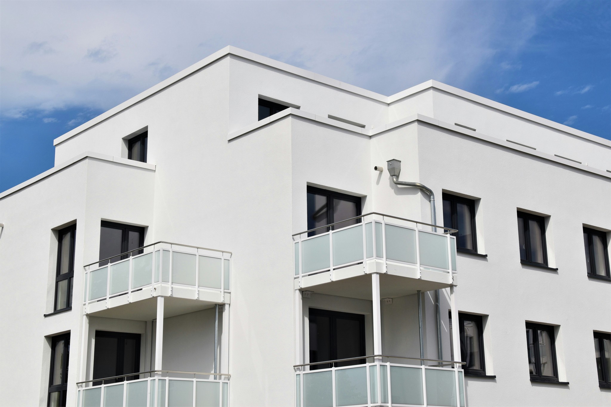 Modern white building with balconies, under a clear blue sky.