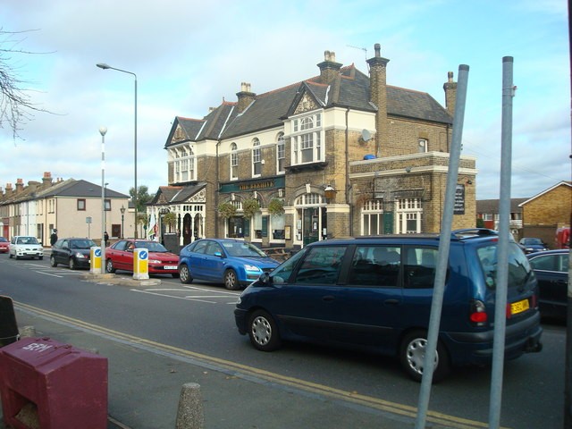A smiling man with curly hair is sitting at a desk, looking at the camera, with a laptop and a lamp in the background.