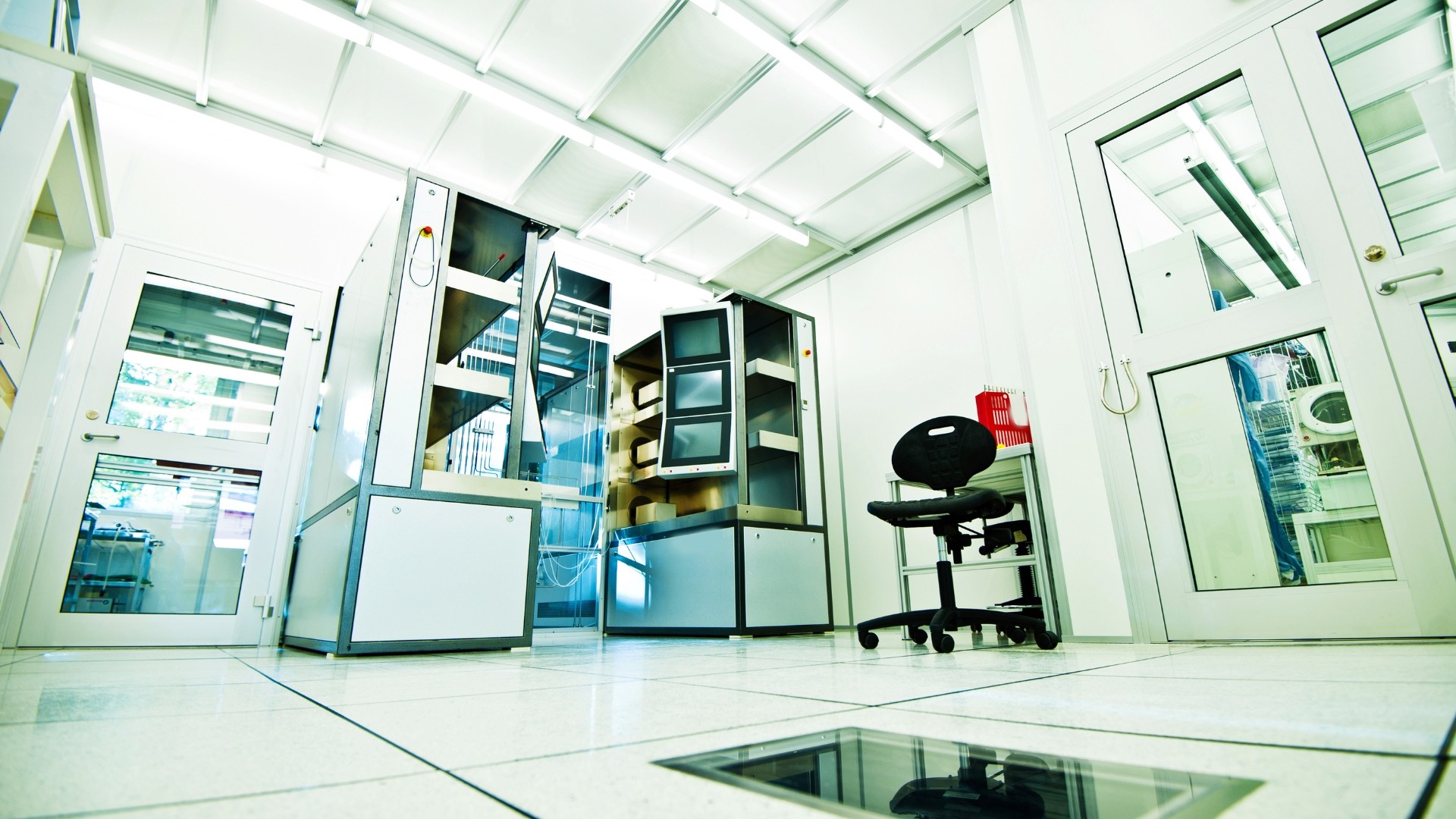 A man stands while two people sit at a table in an office setting, smiling and engaged in conversation. The mood is friendly and collaborative.