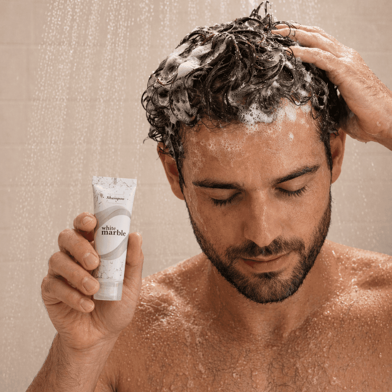 Man in the shower applying White Marble Dial Transmacro Amenities shampoo with foam in his hair and product visible in hand