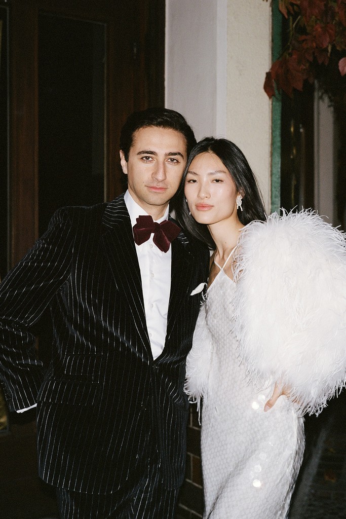 Flash portrait of stylish groom and bride leaning onto each other outside of bar at night