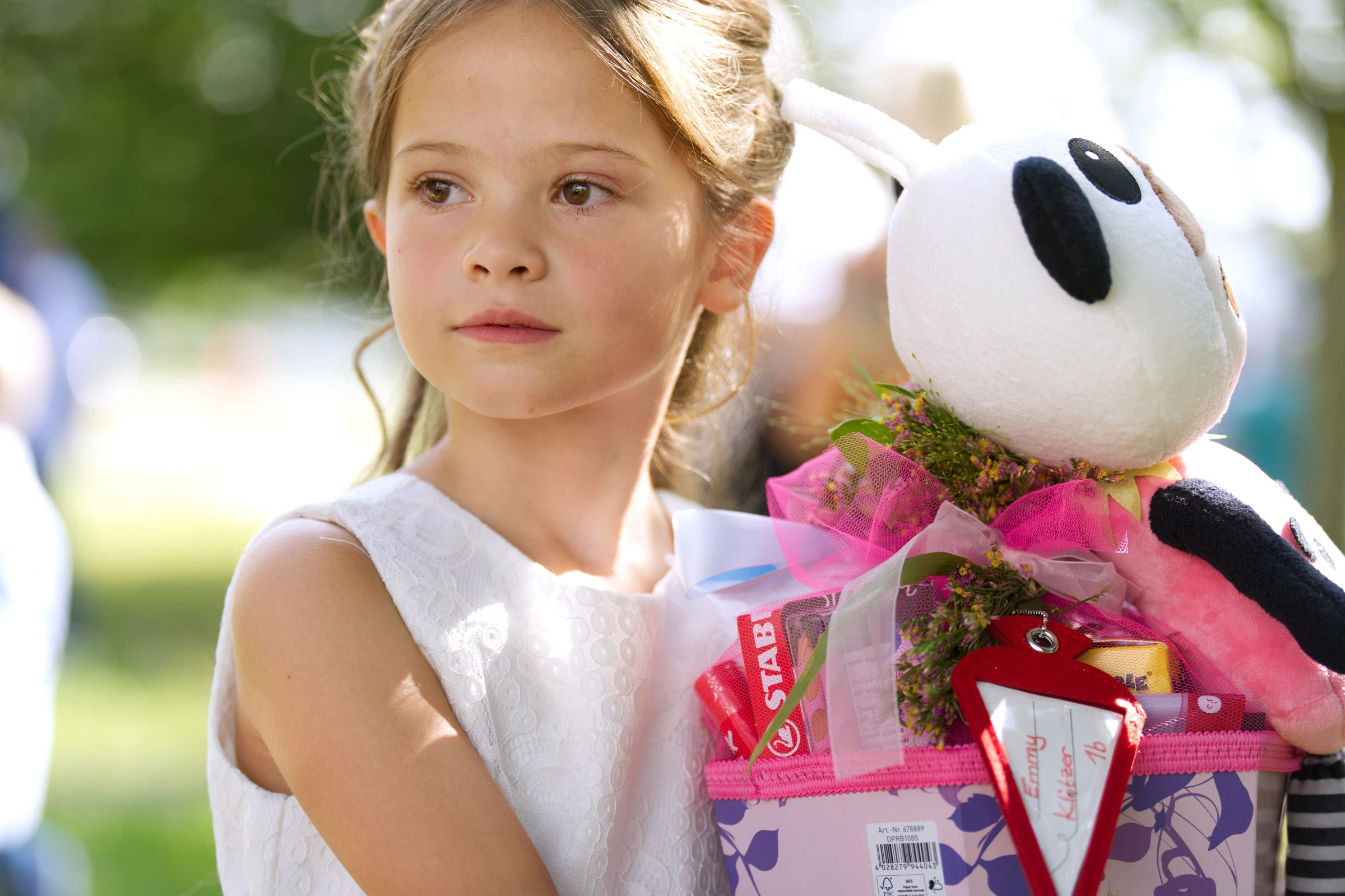 Emmy blickt nachdenklich zur Seite und hält ihre Schultüte fest, während sie die Eindrücke ihrer Schuleinführung erlebt.